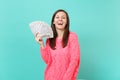 Laughing young woman in knitted pink sweater hold in hand lots bunch of dollars banknotes, cash money isolated on blue