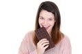 Laughing young woman in knitted pink sweater holding in hand biting and eating chocolate bar on white blank wall Royalty Free Stock Photo