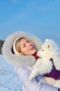 Laughing young woman and samoyed puppy kiss on winter frosty day Royalty Free Stock Photo