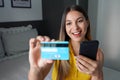 Laughing young woman using telephone for shopping online showing and looking her credit card in her bedroom at home Royalty Free Stock Photo