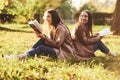 Laughinh brunette twin girls sitting back to back on the grass and having fun with legs slightly bent in knees, with Royalty Free Stock Photo