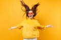 Laughter girl in fur sweater and heart orange glasses fooling around in studio jump with volant hair isolated on bright