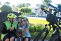 Laughter and love for two elderly people cyclists with yellow helmets making a break in a green park eating a fruit and smiling. Royalty Free Stock Photo