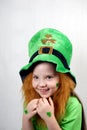 Laughting cute small girl with decorative red beard, green shamrok leaf on her cheek and leprechaun hat, raised her hands with