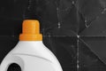 Laundry detergent in a plastic white container with a bright orange screw cap on a background of old crumpled black paper