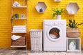 Laundry room interior with modern washing machine near yellow brick wall Royalty Free Stock Photo