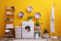 Laundry room interior with modern washing machine near yellow brick wall Royalty Free Stock Photo