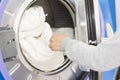 Laundry washing machine. A hand putting or getting some bed sheets from or into the laundry washing machine.