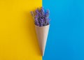 lavender flowers bouquet in parchment paper cone on a yellow and blue isolated background. Copy space. Flat lay. Minimalism. Art Royalty Free Stock Photo