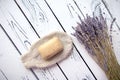 Lavender soap bar on an eco friendly bath mitten along with dried lavender on white wooden background