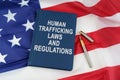 On the US flag lies a pen and a book with the inscription - HUMAN TRAFFICKING LAWS AND REGULATIONS