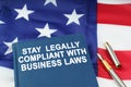 On the US flag lies a pen and a book with the inscription - STAY LEGALLY COMPLIANT WITH BUSINESS LAWS Royalty Free Stock Photo