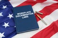 On the US flag lies a pen and a book with the inscription - WORKPLACE DISCRIMINATION LAWS Royalty Free Stock Photo