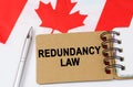 Against the background of the flag of Canada lies a notebook with the inscription - REDUNDANCY LAW