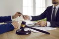 Wooden brown gavel of judge against background of lawyer and client signing legal contract.