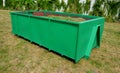 On the lawn is a green tin container for grass clippings from gardens and parks. a man checks the quality and quantity of grass by Royalty Free Stock Photo