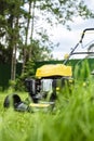Lawn mower on green grass, against a background of trees and a fence, in the yard Royalty Free Stock Photo