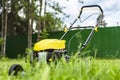 Lawn mower on green grass, against a background of trees and a fence, in the yard Royalty Free Stock Photo