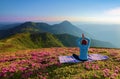 On the lawn among the rhododendron flowers the yoga girl is sitting in the pose on the colorful rug. Meditation. Relax.