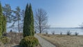 A lawn on the shore of a frozen lake on a sunny spring day. Thuja, trees against a blue sky and an ice-covered lake Royalty Free Stock Photo