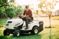 lawnmower tractor with worker doing landscaping works at weekend sunset