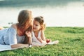 Lay down, the grass is magnificent. Photo of young mother and her daughter having good time on the green grass with lake