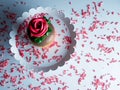 Lay flat photography picture of a yellow cupcake decorated with chocolate frosting and a red rose on a white platter with red and