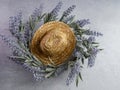 Lay flat photography of a straw cowgirl or cowboy hat sitting on top of a purple lavender flower plant wreath against a white gray