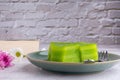 Layer sweet cake or khanom Chan on a plate with a book and flowers on gray stone background with white brick wall