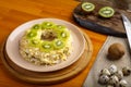 Layered salad with chicken and kiwi with nuts next to quail eggs on a kiwi napkin on a board and a knife on the table.