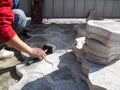 Laying gray paving tiles `Bikini` in the yard. There are part of the body of a man with a rubber hammer in his hand and a stack