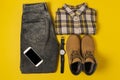Layout of autumn clothes and accessories in warm colors on a yellow background. Jeans, shirt, boots, phone and watch flat lay