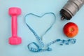 Layout on a blue background. Dumbbell, heart shaped measuring tape, bottle and apple. Fitness symbols Royalty Free Stock Photo