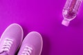 Violet sneakers with a bottle of water on a purple background.