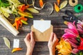 Layout greeting card. Woman`s hands holds envelope with blank sheet and flowers decorations on wooden table Royalty Free Stock Photo