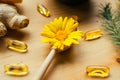 Yellow calendula flower in wooden spoon, fish oil capsule, lemon, , and ginger at wooden table