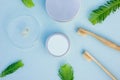 Layout of round silver cans, bamboo toothbrushes, glass cup with organic tooth paste and few green leaves. Zero waste hygiene