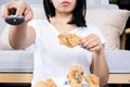 Lazy Asian woman eating fried chicken hand holding remote tv, unhealthy lifestyle concept