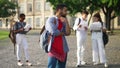 Lazy bored Middle Eastern student standing outdoors at university campus with nerds groupmates learning at background