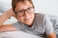 A lazy cheerful happy boy wearing glasses lying in bed and resting, because he is not in school during lockdown or