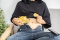 Lazy girl eating unhealthy , fast food hand holding bowl of potato chips sitting on sofa watching tv Royalty Free Stock Photo
