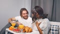 Lazy morning in bed. Young multiethnic couple drinking juice and having a breakfast in the hotel room on honeymoon Royalty Free Stock Photo