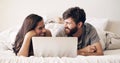 Lazy mornings online. Shot of a happy young couple using a laptop while relaxing on the bed at home.