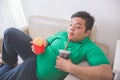 Lazy obese person eats junk food while laying on a couch