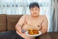 Lazy overweight asian male with fast food and watching televisio
