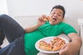 Lazy overweight man eating pizza while laying on a couch Royalty Free Stock Photo