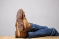 Lazy person concept: man`s legs wearing blue jeans of desert boots rest on a wooden table with copy space for your text