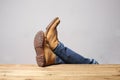 Lazy person concept: man`s legs wearing blue jeans of desert boots rest on a wooden table with copy space for your text