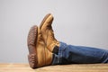 Lazy person concept: man`s legs wearing blue jeans of desert boots rest on a wooden table with copy space for your text