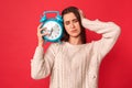 Lazy to Wake Up. Young woman standing isolated on red with alarm clock touching head unhappy